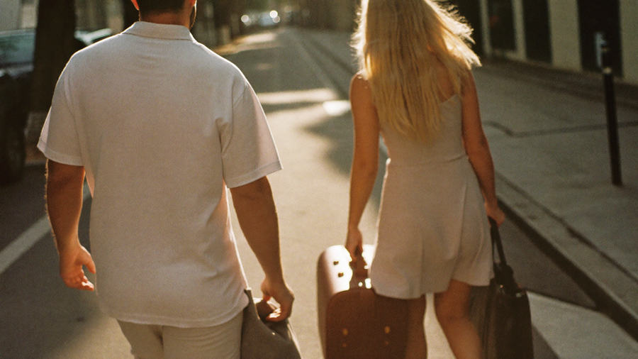 Couple s'eloignant dans une rue au soleil couchant, sacs de voyage a la main