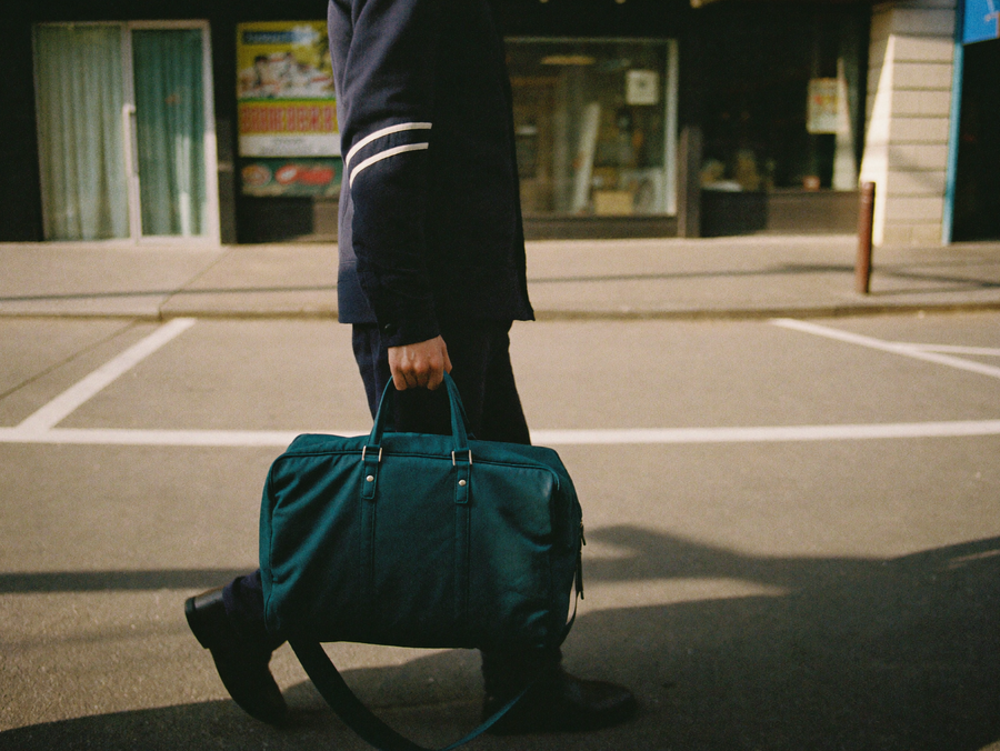 Homme portant un sac de voyage bleu canard a la main dans la rue